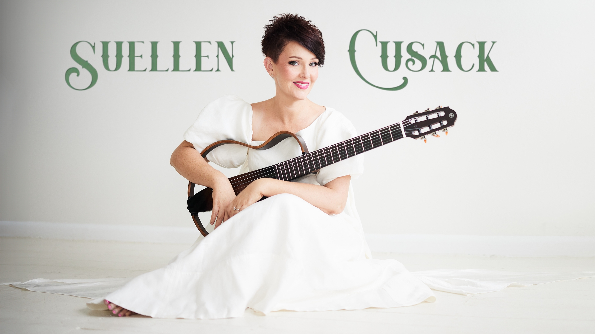 Suellen Cusack sitting in a white gown holding her guitar